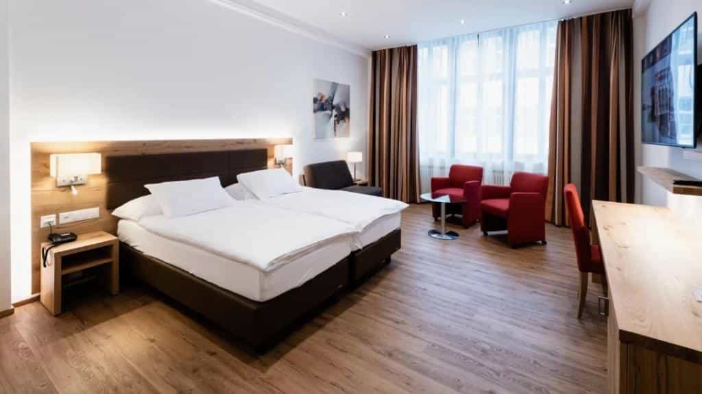 Hotel room with twin beds, wood floors, seating area, and large window with striped curtains.