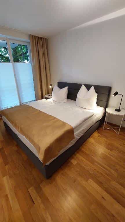 Bedroom with large bed, white linens, brown runner, and hardwood floors near window.