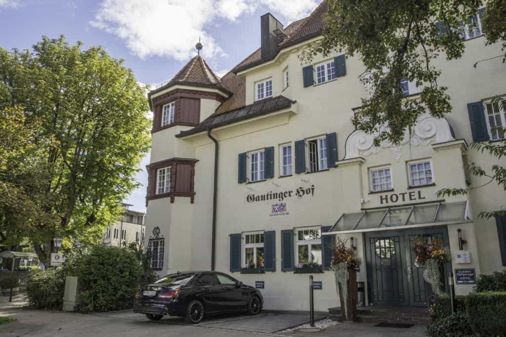 Gautinger Hof Hotel entrance with black car parked outside near green trees.