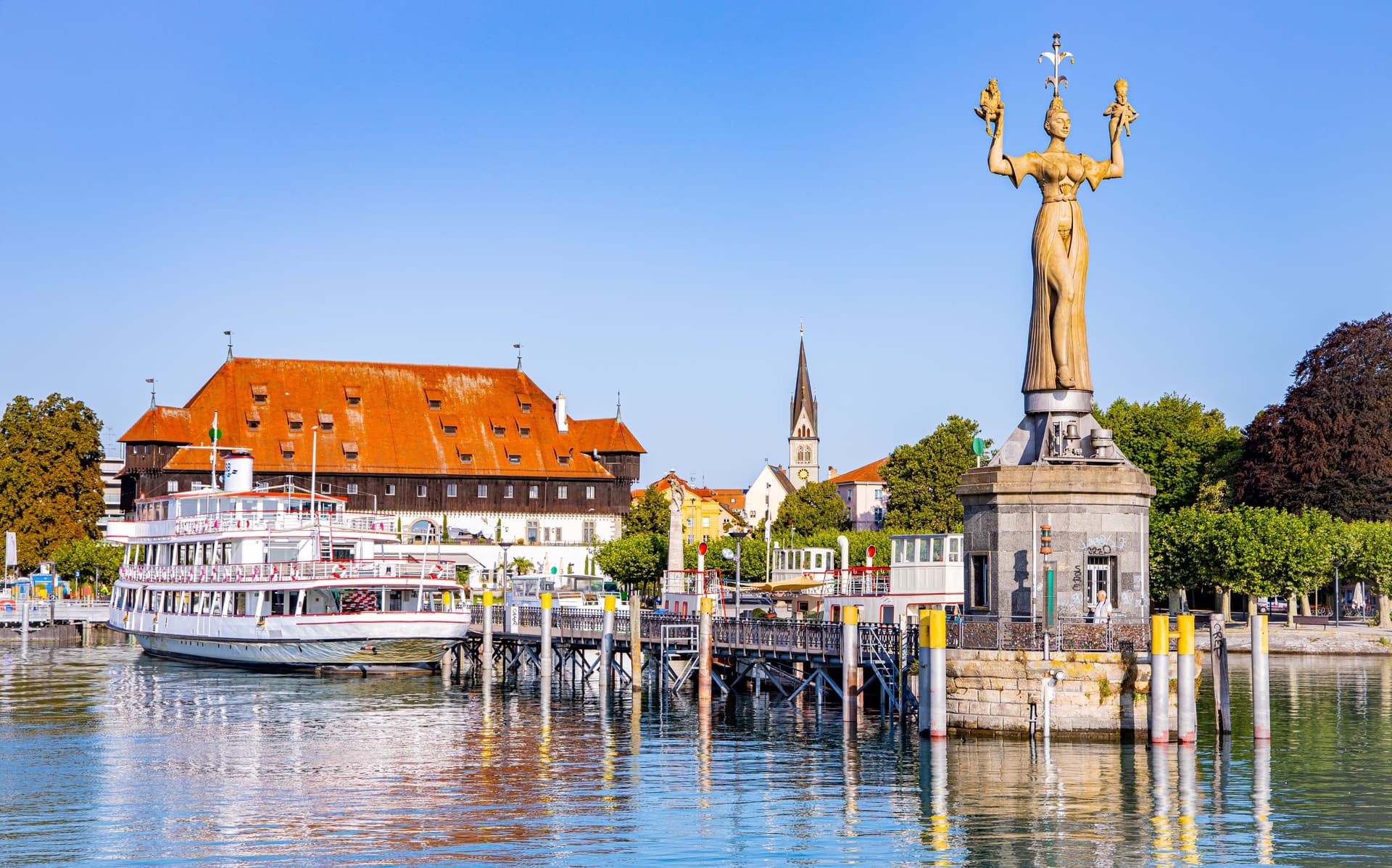 Constance statue on the water with a white passenger boat and historic buildings.