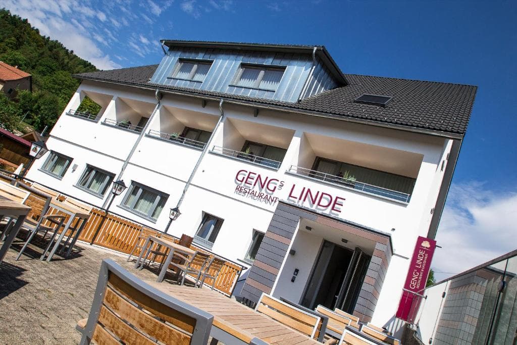 Hotel Gengs Linde restaurant exterior with outdoor seating and forested hill under blue sky.