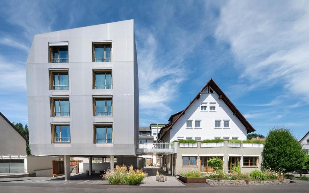 Modern hotel next to traditional white building under blue sky in Constance.