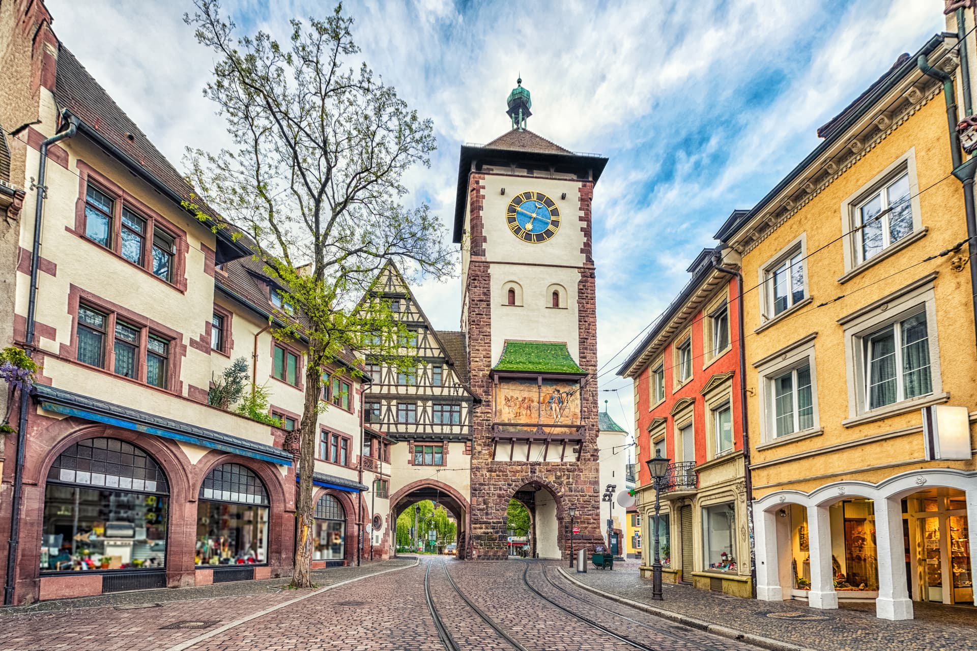 Cobblestone street leading to the Martinstor clock tower in Freiburg center with tram tracks.