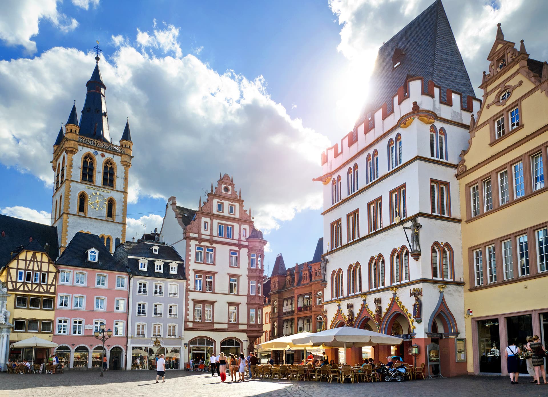 Historic square in Trier with colorful buildings and a prominent clock tower under a bright, cloudy sky.