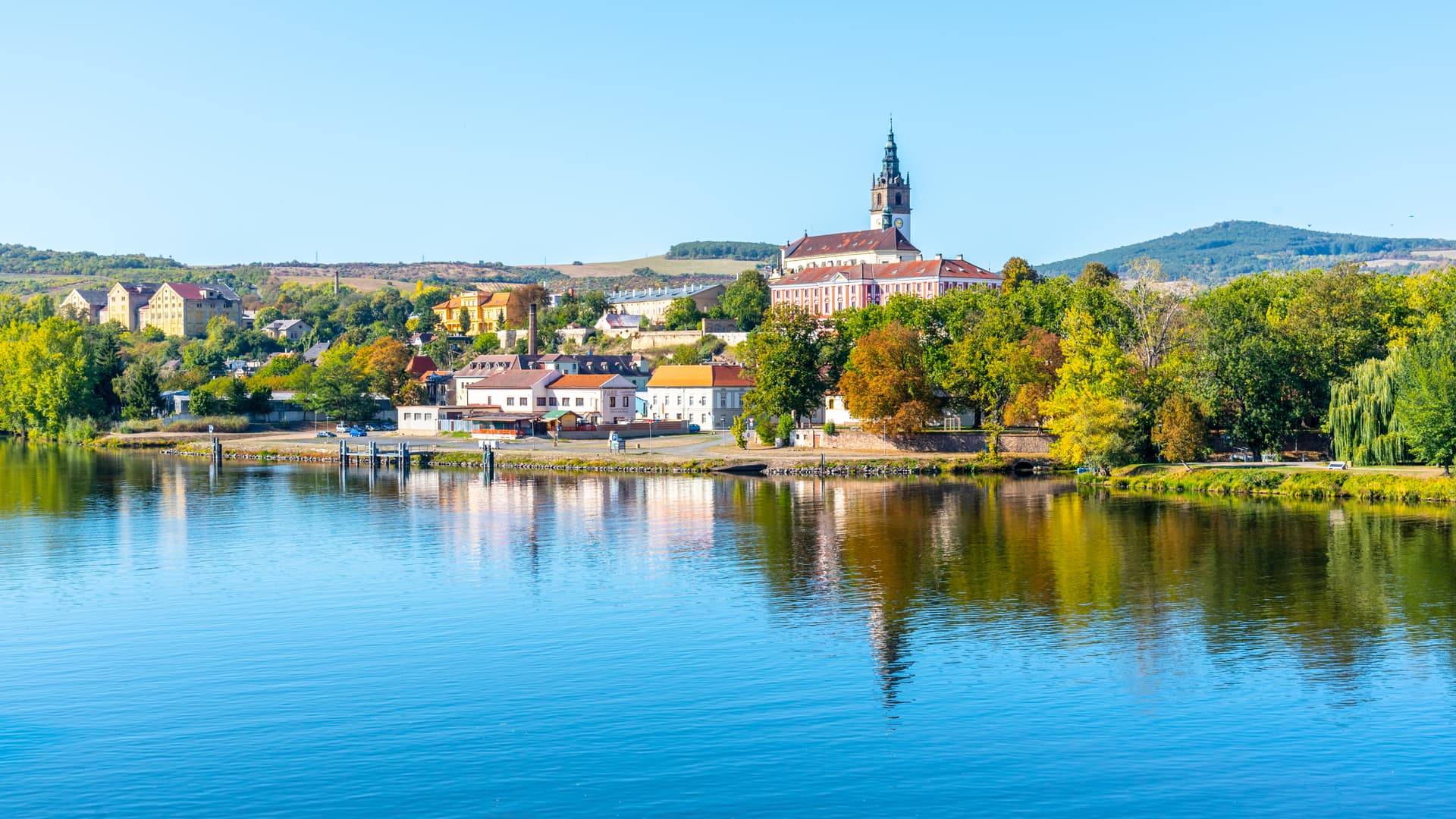 Riverfront view of Litoměřice town with a prominent church tower reflected in the blue water.