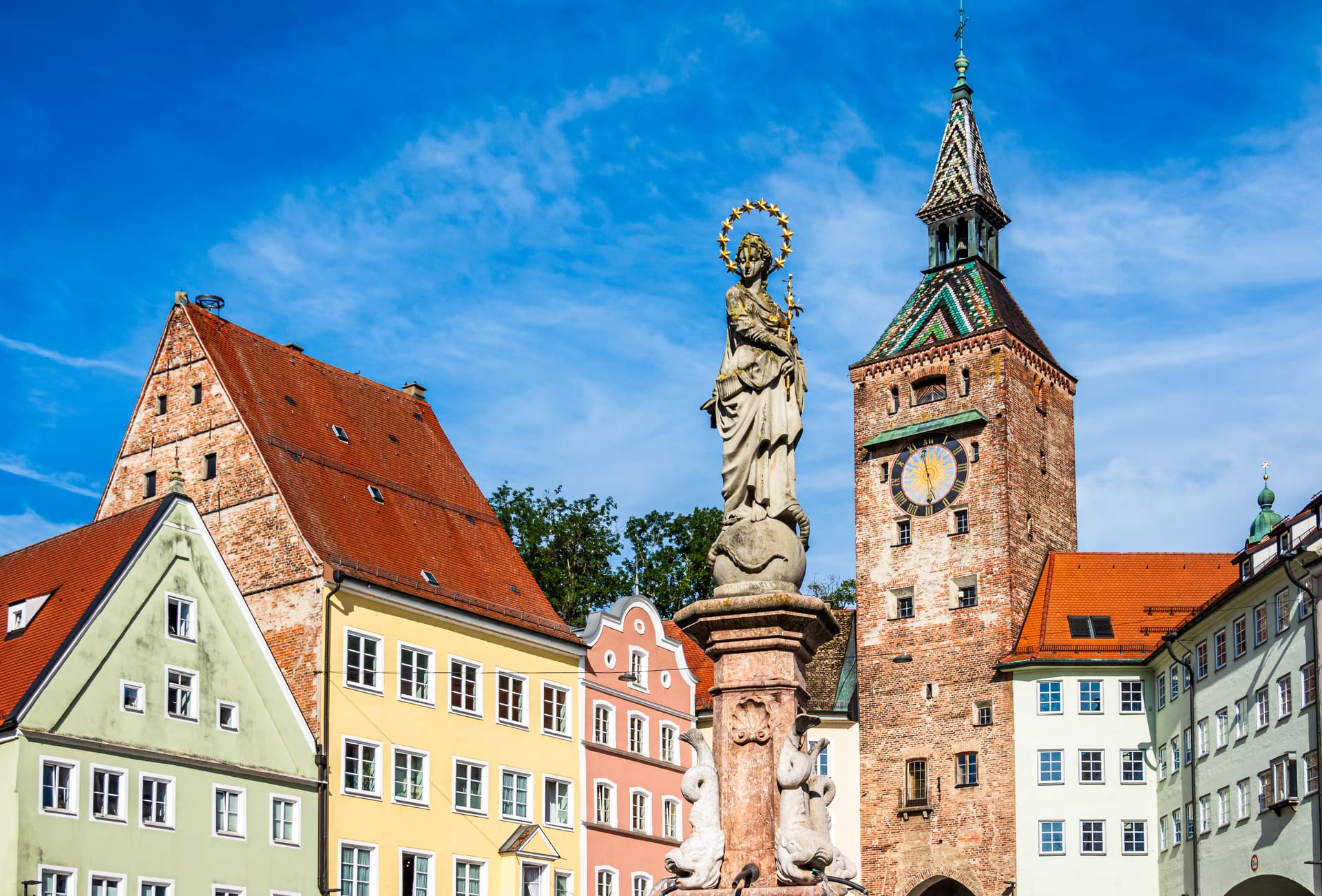 Statue on fountain before colorful historic buildings and brick clock tower in Landsberg.