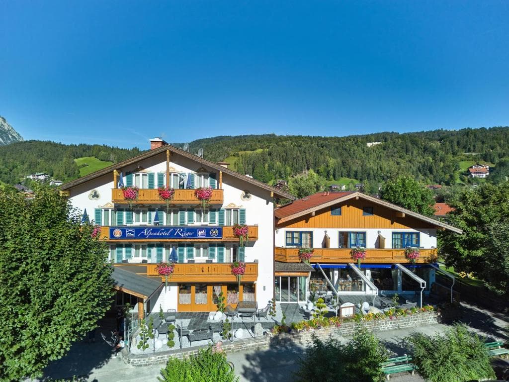 Alpenhotel Rieger in Wallgau with balconies and outdoor seating against a backdrop of green mountains.