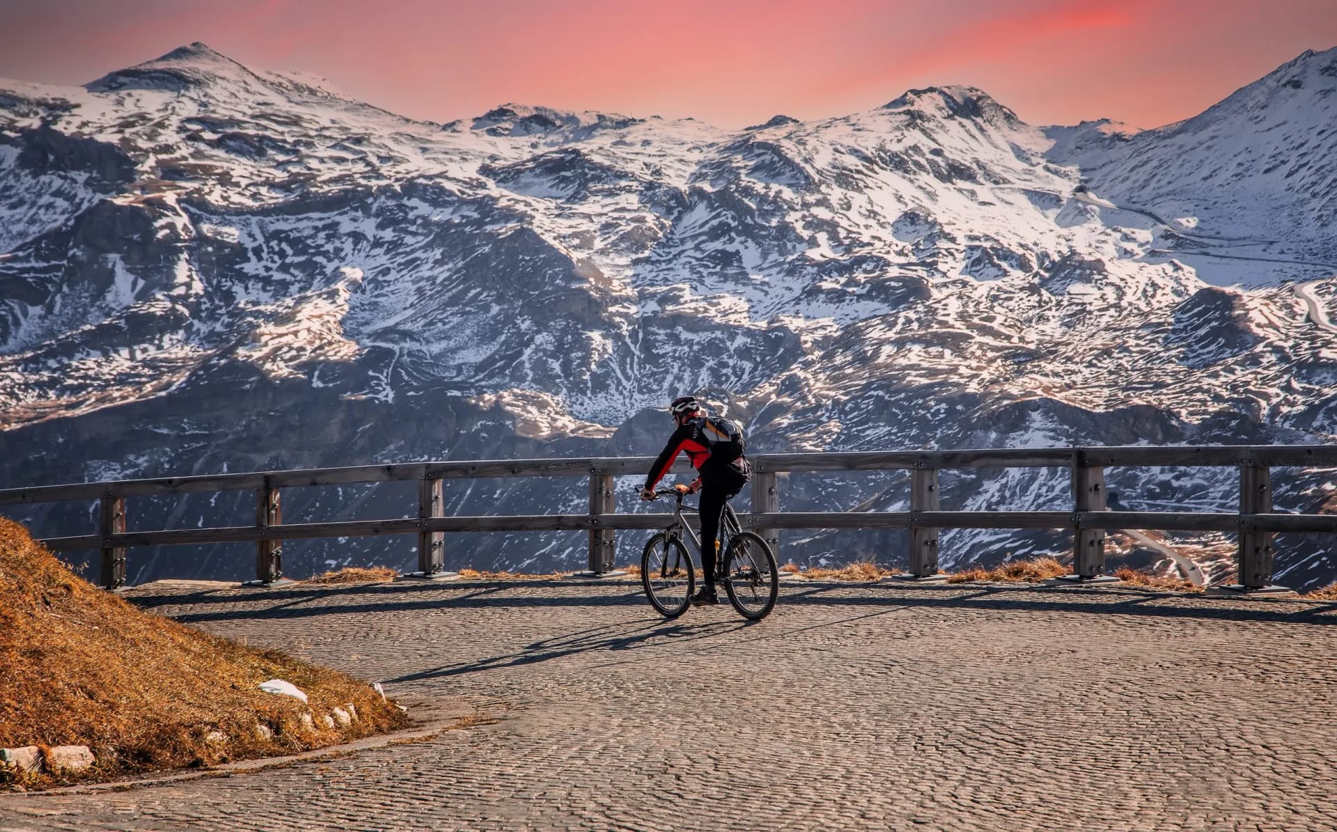 Cyclist on cobblestone road overlooking snow-capped mountains at sunset