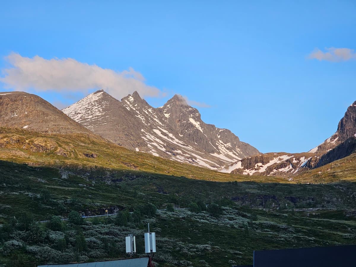 Rugged mountains with snow patches above green, scrubby foothills under a blue sky.
