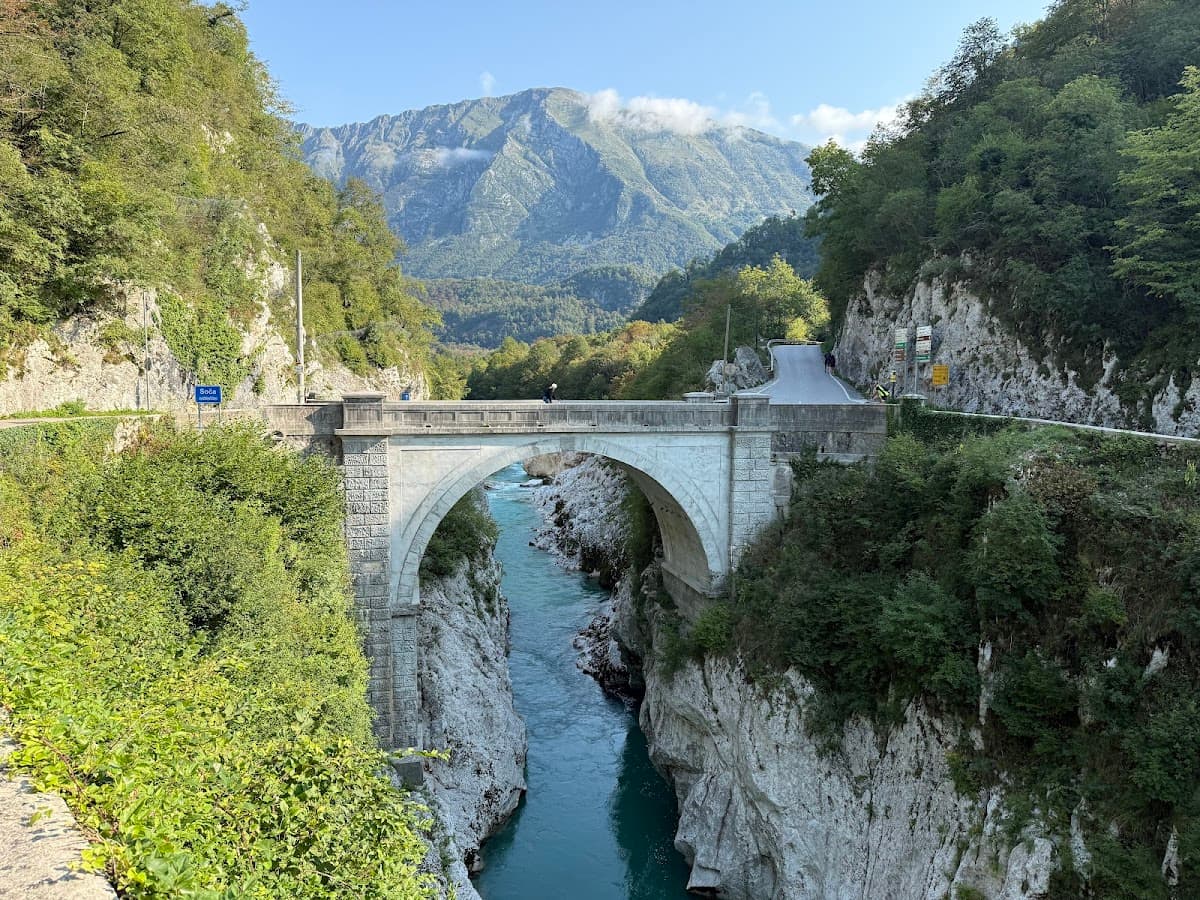 Stone arch bridge over turquoise river canyon with lush green mountains in background