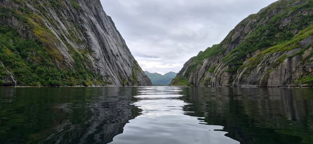 Fjord with steep rocky cliffs and calm water under cloudy sky