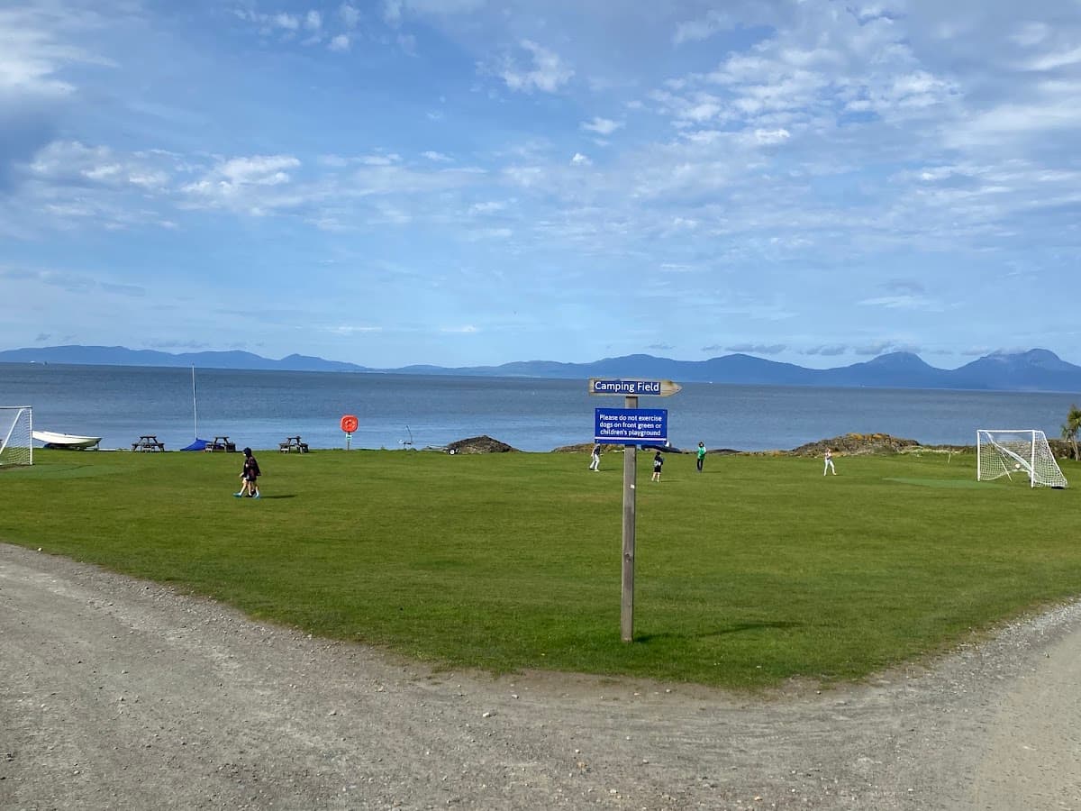 Green grassy field by the sea with soccer goals and sign pointing to camping field
