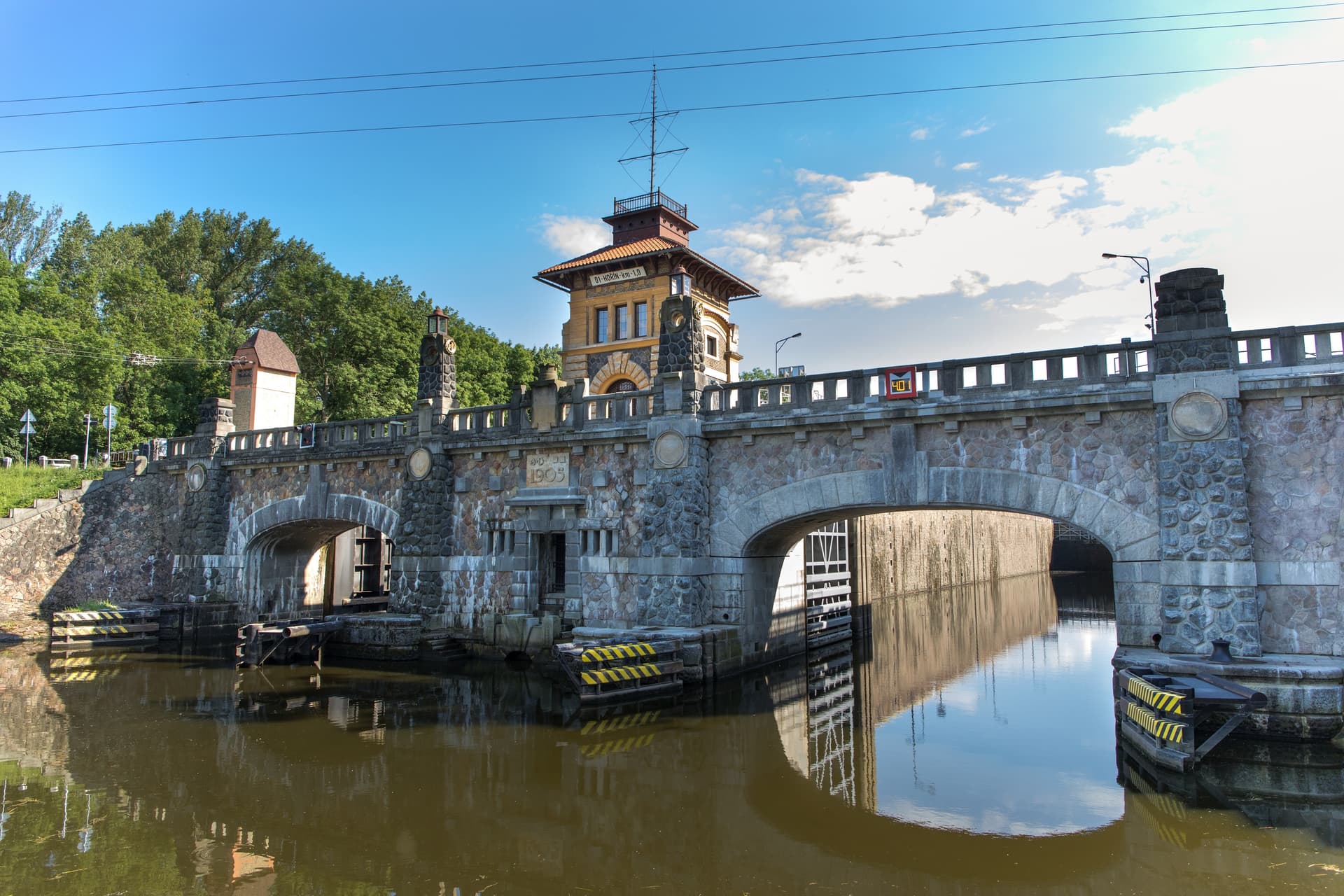Stone bridge structure with central building and arches over murky water, Melnik.