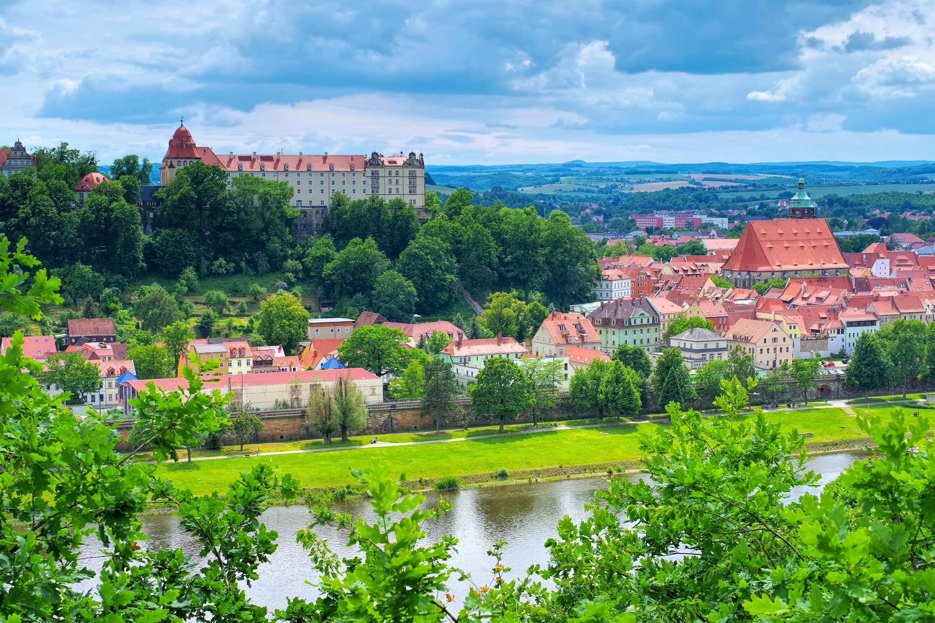 Historic town of Pirna with castle on hill overlooking river and green landscape.