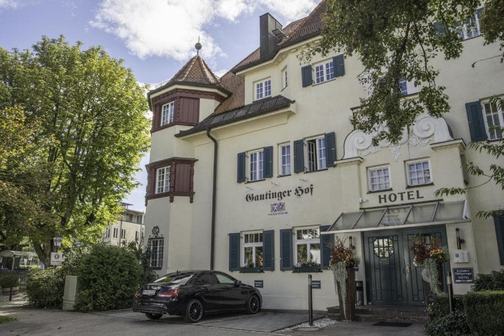 Gautinger Hof Hotel entrance with black car parked outside near green trees.