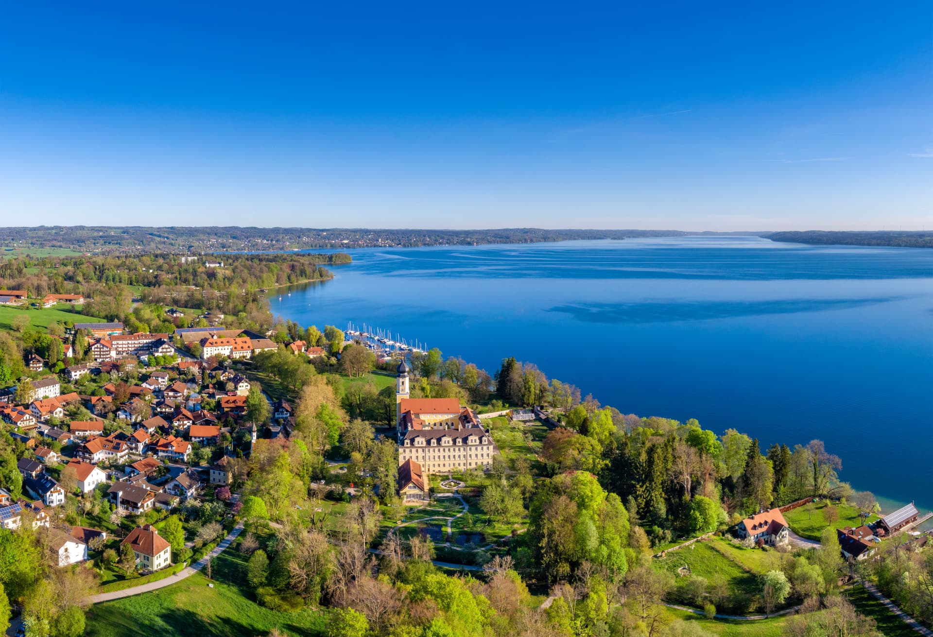 Aerial view of Starnberg town and lake with bright blue water and green spring foliage.