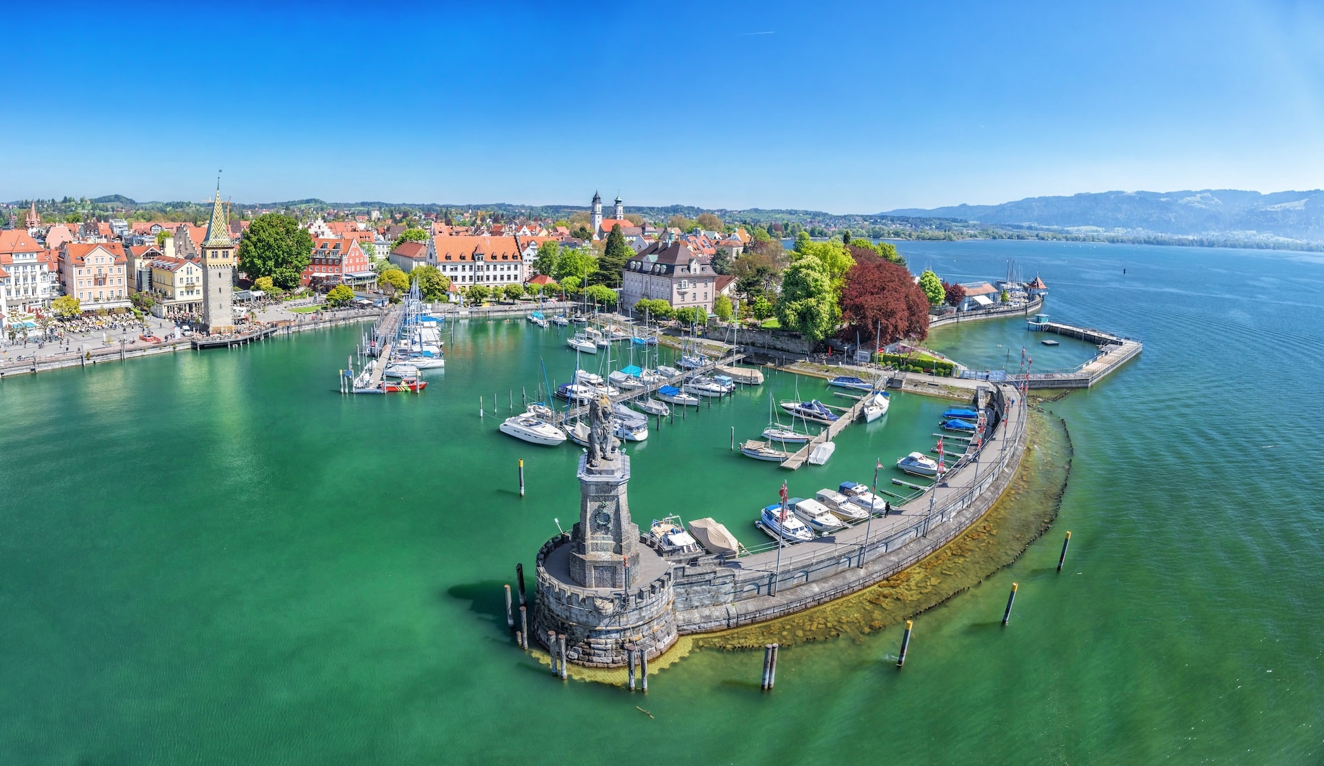 Harbor on Lake Constance with lion statue entrance, Lindau, Bavaria, Germany, and distant mountains.