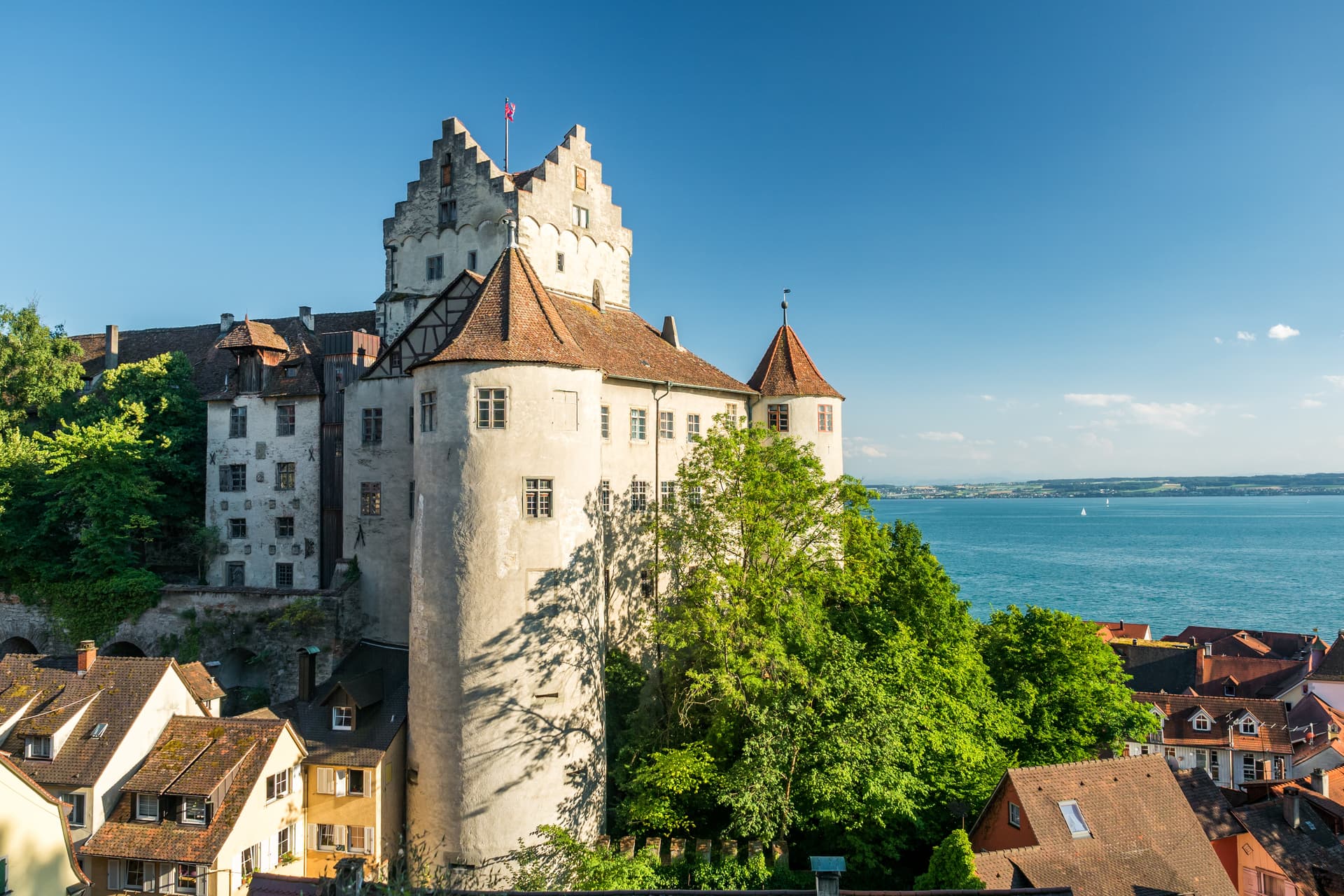 Meersburg Castle overlooking red-roofed town and blue Lake Constance under clear sky.
